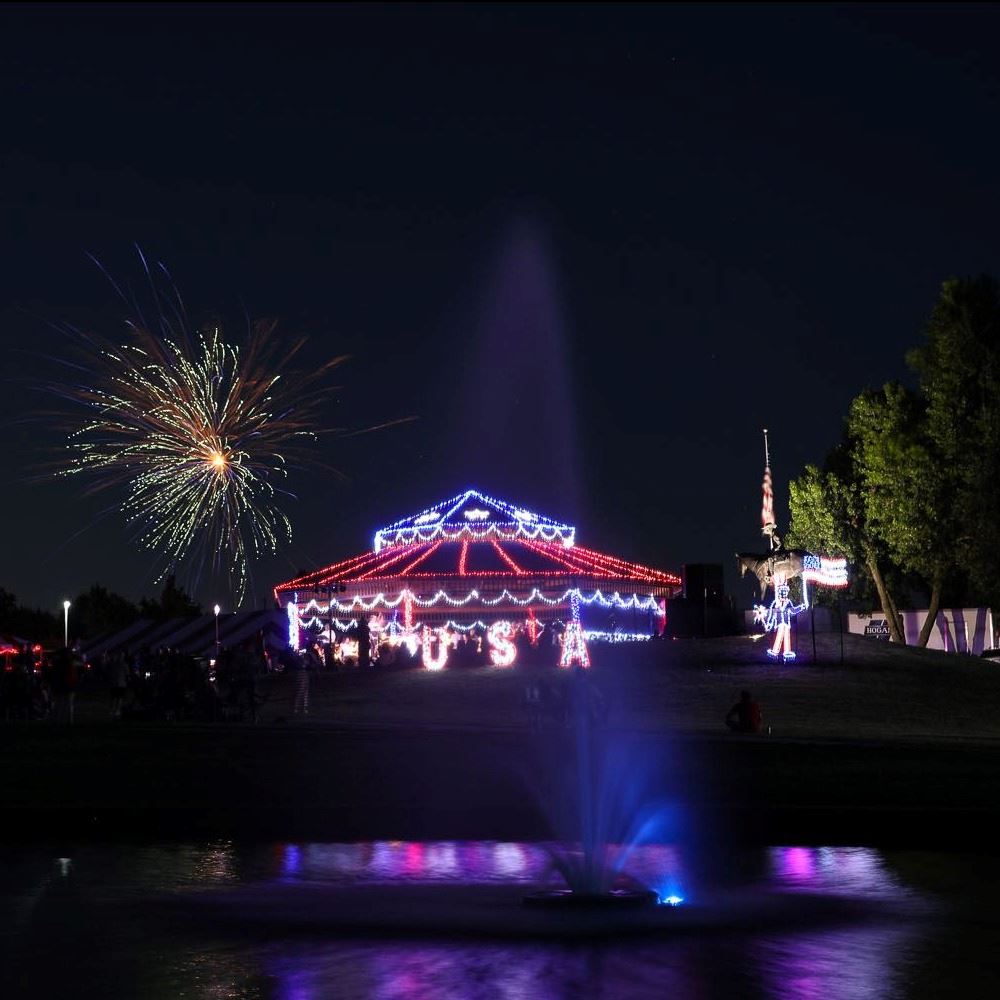 Lights twinkle on a gazebo at Freedom Fest as Fireworks ignite in the sky above.