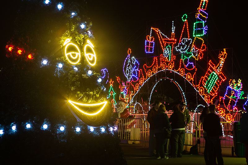 People Converse Next to a Nearby Christmas Tree with a Face on It